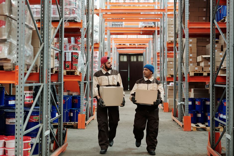 Warehouse workers carrying boxes down a storage aisle