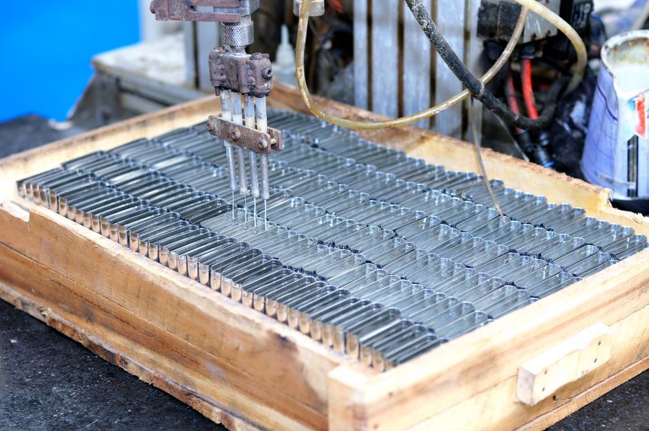 Metal components arranged in a tray under an automated dispensing head