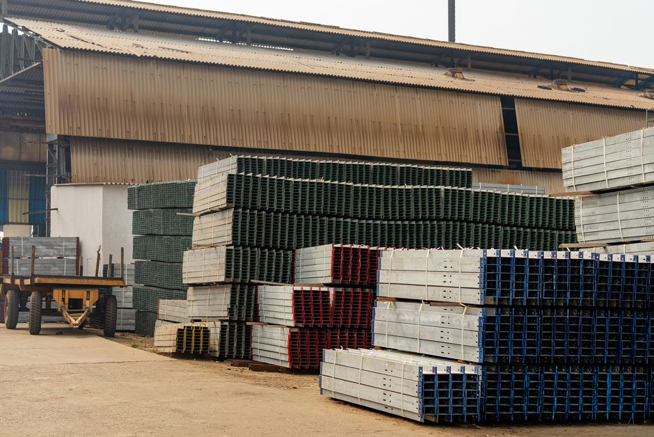Bundled steel sections stacked in a yard outside a plant shed